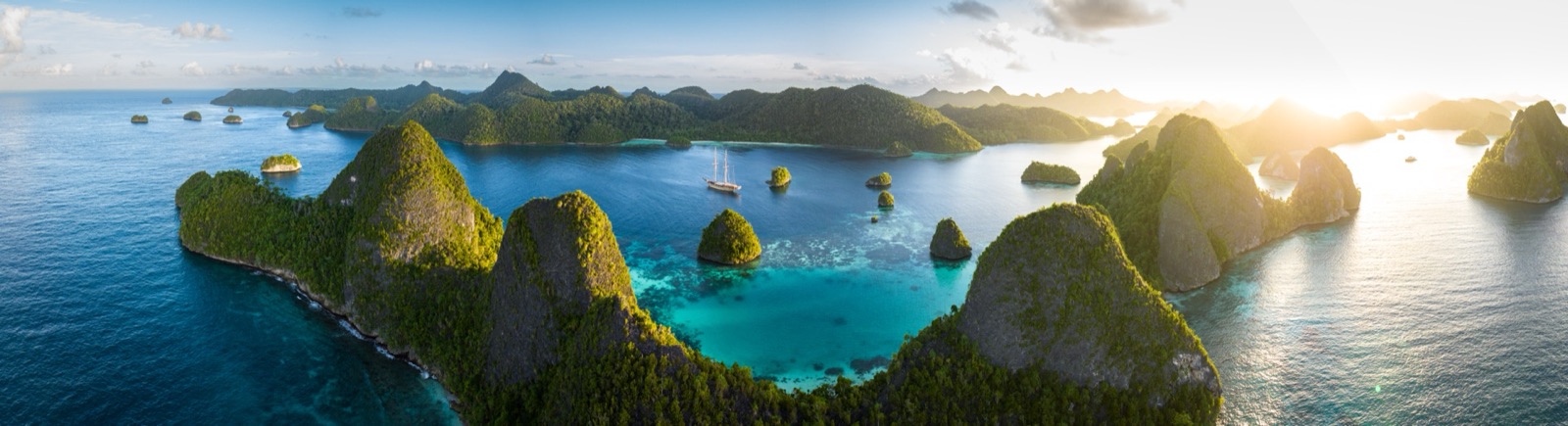 A classic schooner anchored beyond a palm — tropical archipelago.